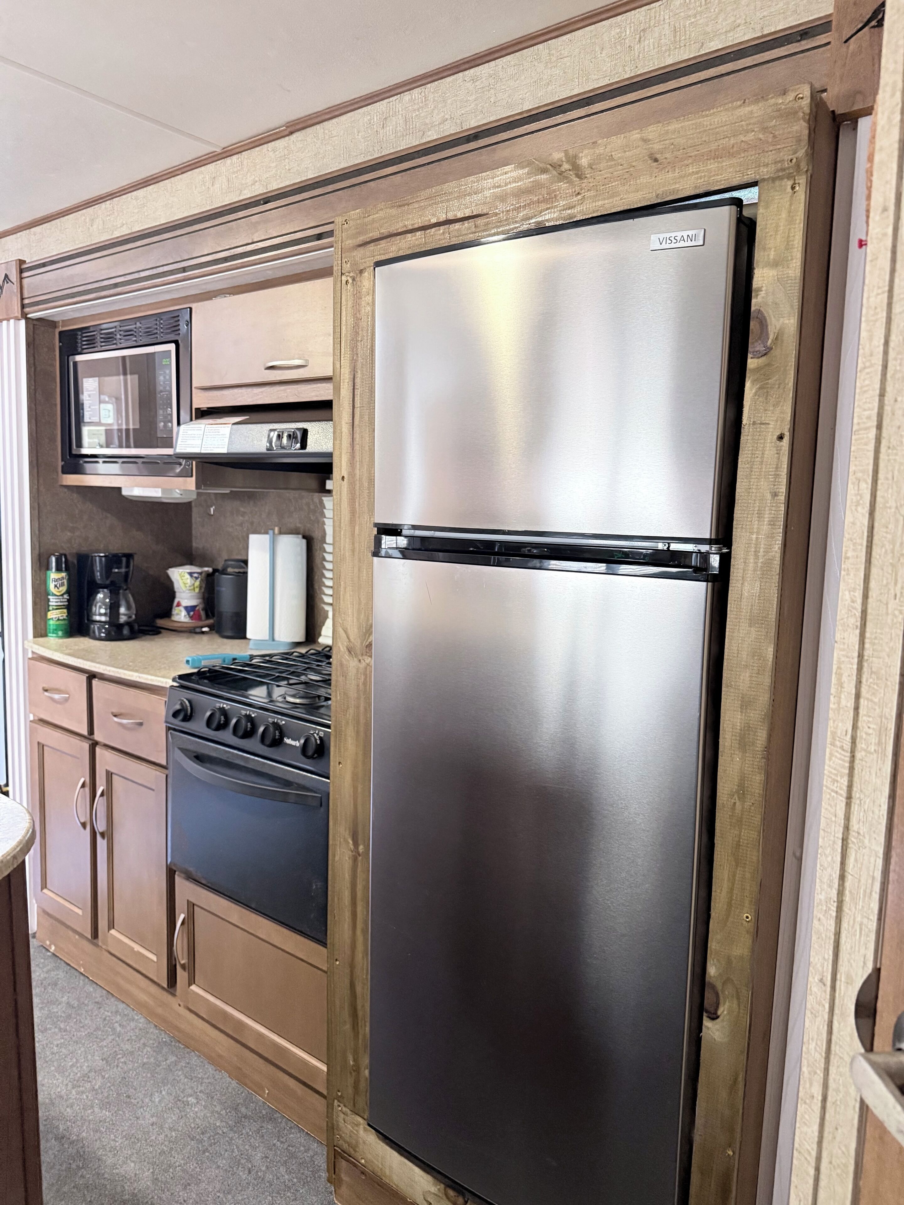 Una kitchenette compacta con refrigerador de acero inoxidable, microondas, estufa y armarios de madera.