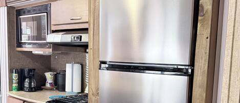 Una kitchenette compacta con refrigerador de acero inoxidable, microondas, estufa y armarios de madera.