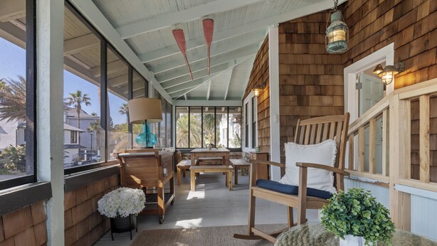 A covered porch with wooden furniture, a potted plant, and a view of palm trees outside. - Beach Cottage II, near the beach, TPC Sawgrass, Mayo Clinic & Ponte Vedra Beach (Jacksonville Beach)