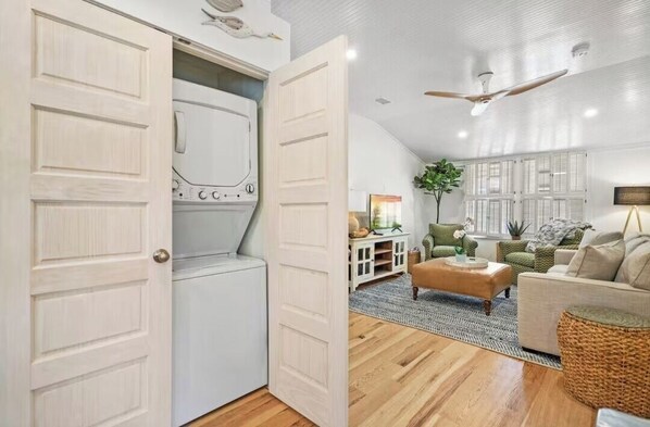 A spacious living area with a high ceiling, a ceiling fan, and a large window with shutters.