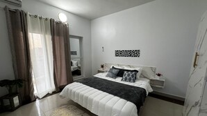Ein Schlafzimmer mit einem Bett, Nachttischen, einem Spiegel, Vorhängen und einer Wandleuchte.