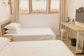 Ein Hotelzimmer mit zwei Einzelbetten, einem Schreibtisch mit Stuhl, einem Fernseher und einem Fenster mit Vorhängen.