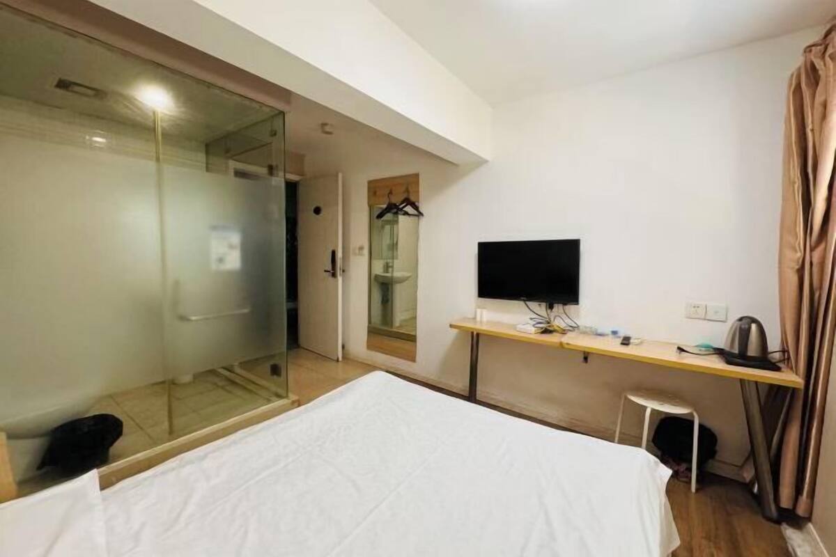 A hotel room with a bed, a desk, a television, and a glass shower enclosure.
