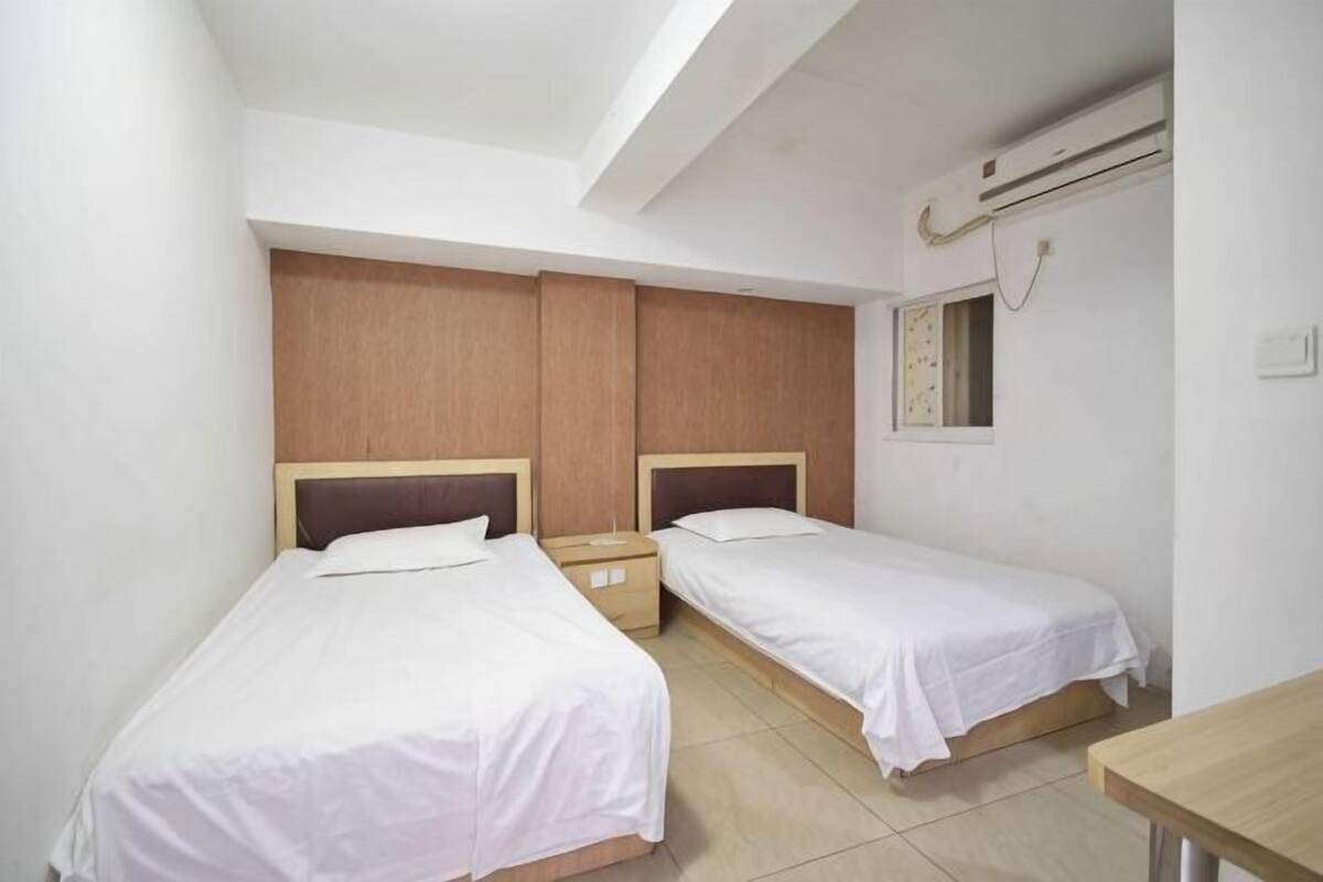A room with two single beds, wooden headboards, a small table, and a window with a view.