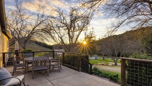 An outdoor patio with a table and chairs, a railing, and a view of trees and a sunset. - Luxury Wine Country Haven Vineyard Views Near Top Wineries Adelaida Farmhouse (Paso Robles)