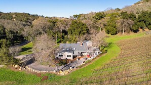 A house with a large driveway, surrounded by a vineyard, and a hilly landscape in the background. - Luxury Wine Country Haven Vineyard Views Near Top Wineries Adelaida Farmhouse (Paso Robles)