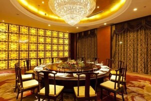 A round dining table with chairs, a chandelier, and a patterned wall.