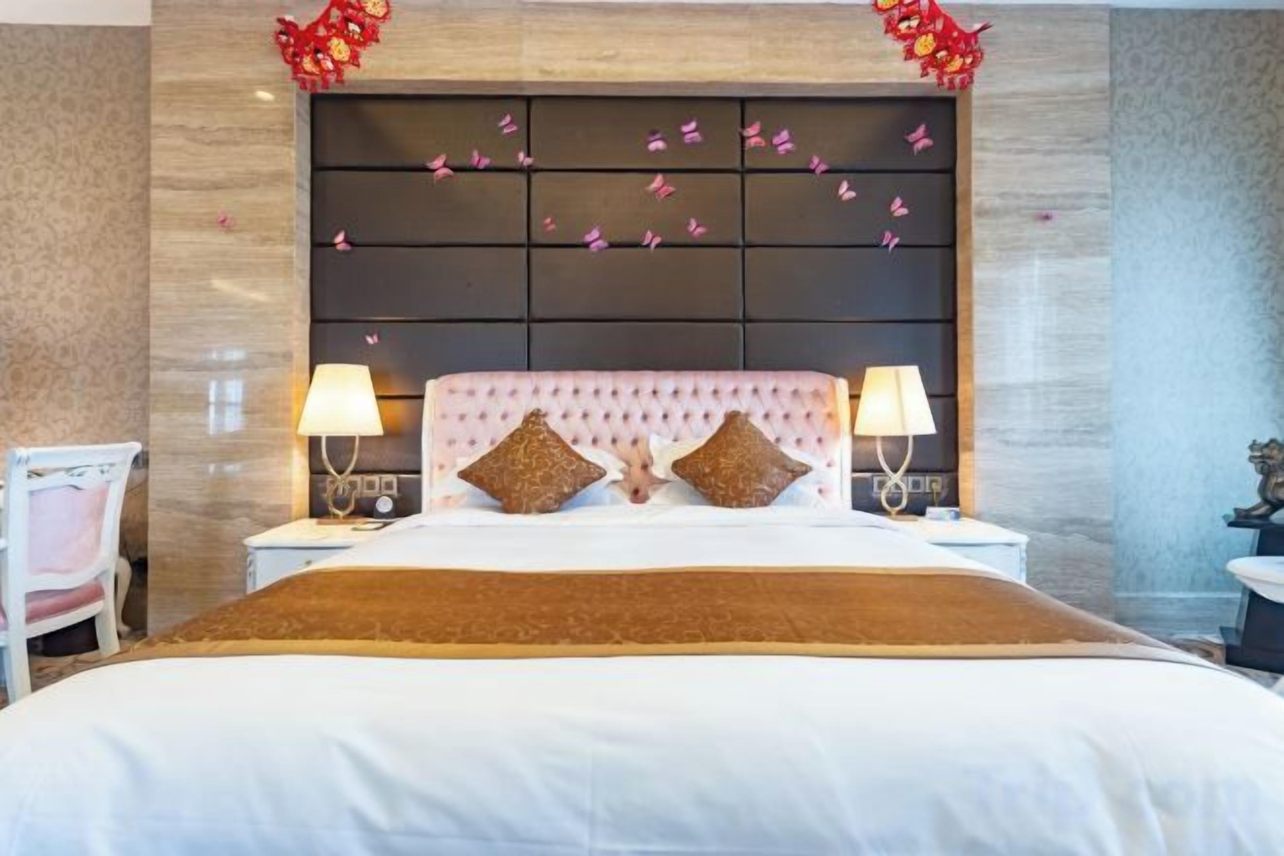 Una camera d'albergo con un letto grande, due comodini, una sedia e una testiera decorativa.