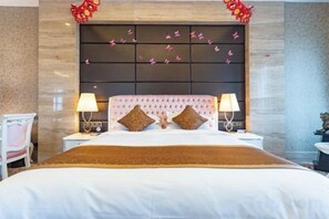 Quarto de hotel com cama grande, duas mesas de cabeceira, uma cadeira e cabeceira decorativa.