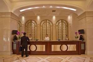 A reception area with a marble reception desk, a man standing to the left, and two receptionists behind the counter. - Jinling International Hotel (Guangrao)