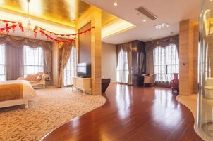 A spacious hotel room with a large bed, a flat-screen TV, a seating area, and a large window.