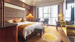 Habitación de hotel con una cama grande, dos lámparas de noche, un escritorio con silla y un ventanal con cortinas.