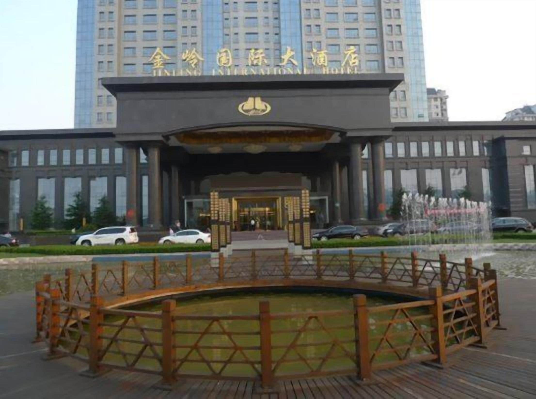 Entrada de hotel con un edificio grande al fondo, una puerta cerrada y un pequeño elemento acuático al frente.