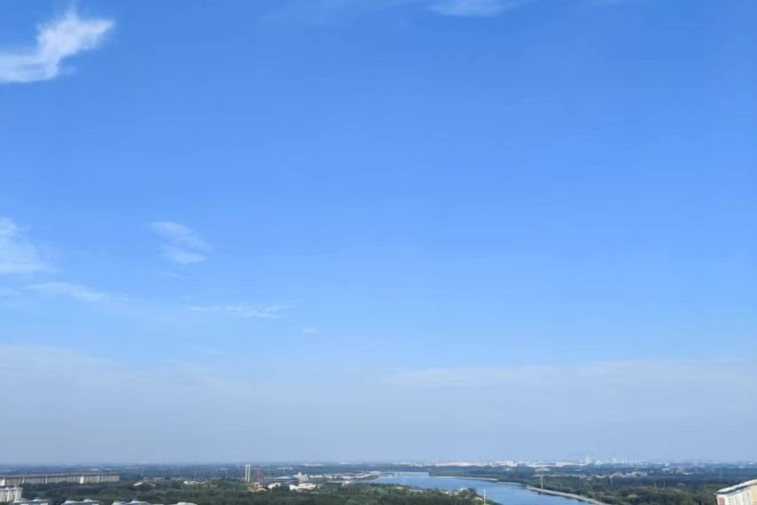 Un ciel d’un bleu limpide, avec une vue lointaine d’une rivière et de bâtiments.