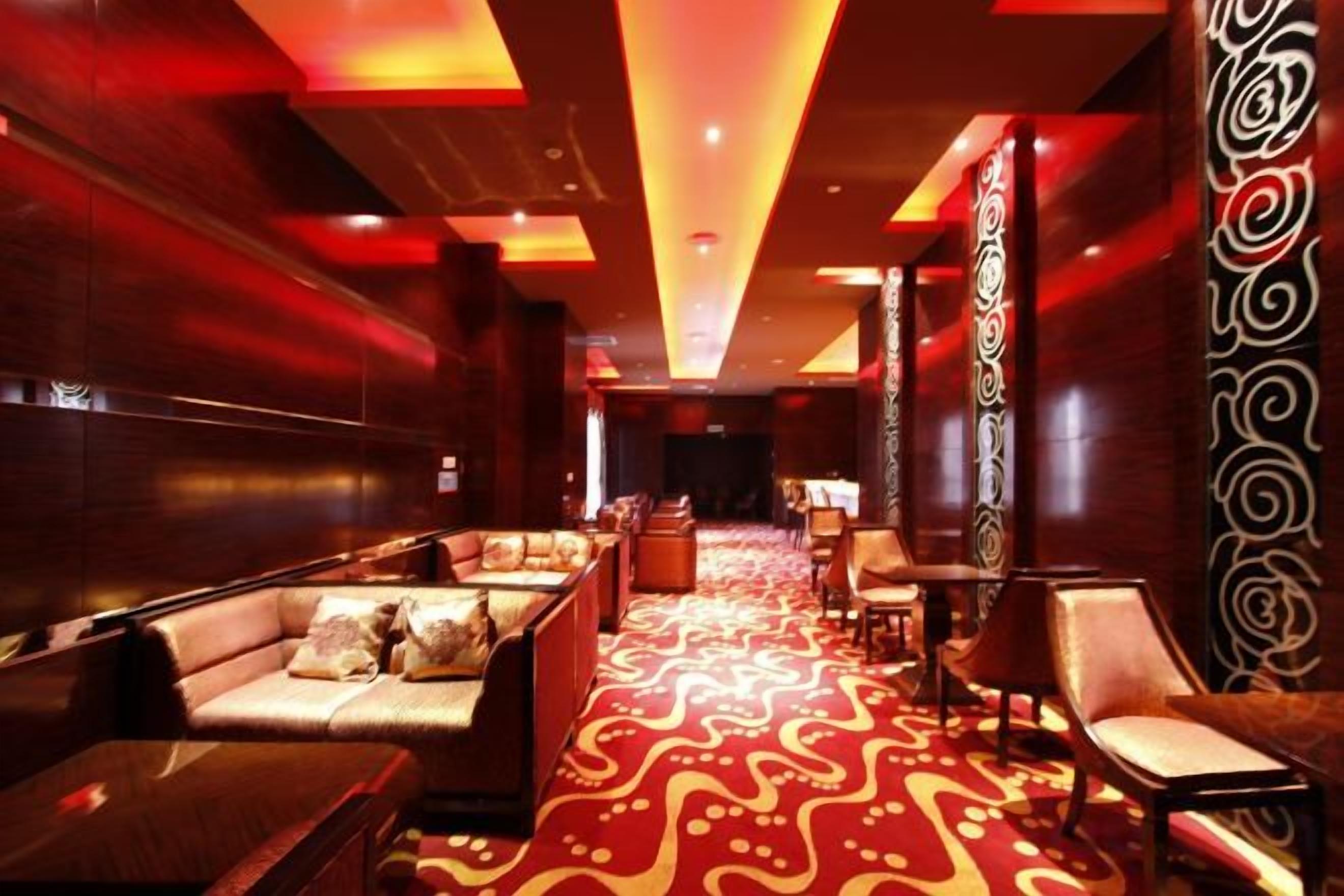 A hotel lobby with a red carpet, seating area, and decorative wall panels.