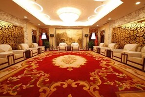 Une salle de conférence avec un tapis rouge, des canapés et un lustre.