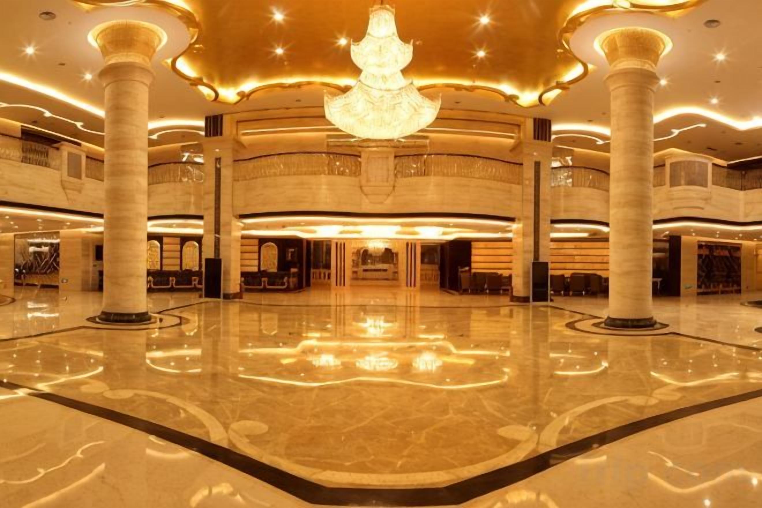A spacious lobby with a central chandelier, multiple columns, and a polished floor.