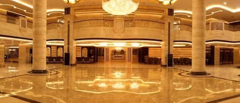 A spacious lobby with a central chandelier, multiple columns, and a polished floor.