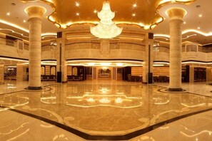 Un hall d’entrée spacieux, agrémenté d’un lustre central, de nombreuses colonnes et d’un sol poli.
