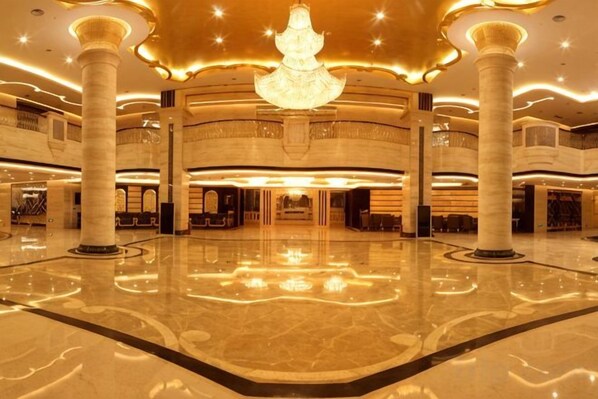 A spacious lobby with a central chandelier, multiple columns, and a polished floor.