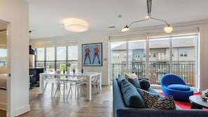 A modern living room with a sofa, a dining table with chairs, and large windows.