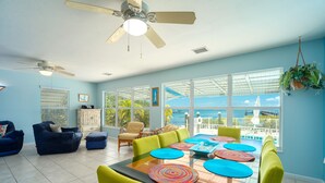 A spacious living area with a dining table, chairs, and a ceiling fan.