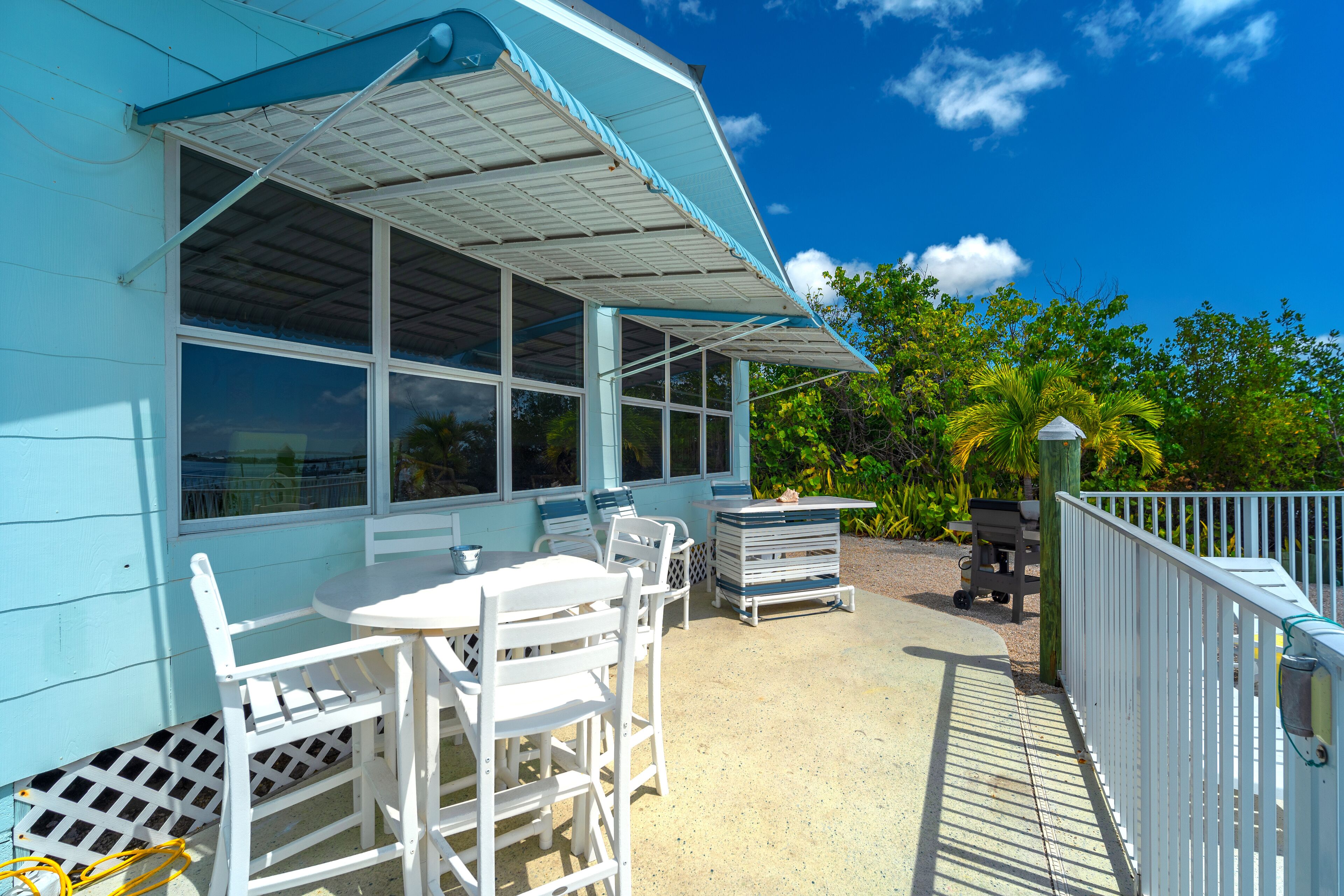 A covered patio area with white furniture, including a table and chairs, and a small grill.