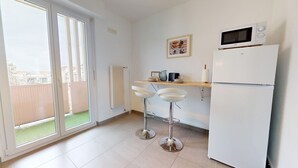 A kitchen with a refrigerator, microwave, and a small table with chairs. There is a sliding glass door leading to a balcony. - La belle étape + 1 parking (Colmar)