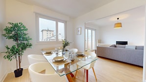 A modern apartment with a dining area featuring a glass table and chairs, a grey sofa, and a potted plant. - La belle étape + 1 parking (Colmar)