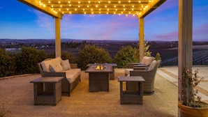 Un patio al aire libre con mobiliario de mimbre, un brasero y una pérgola con luces colgantes.