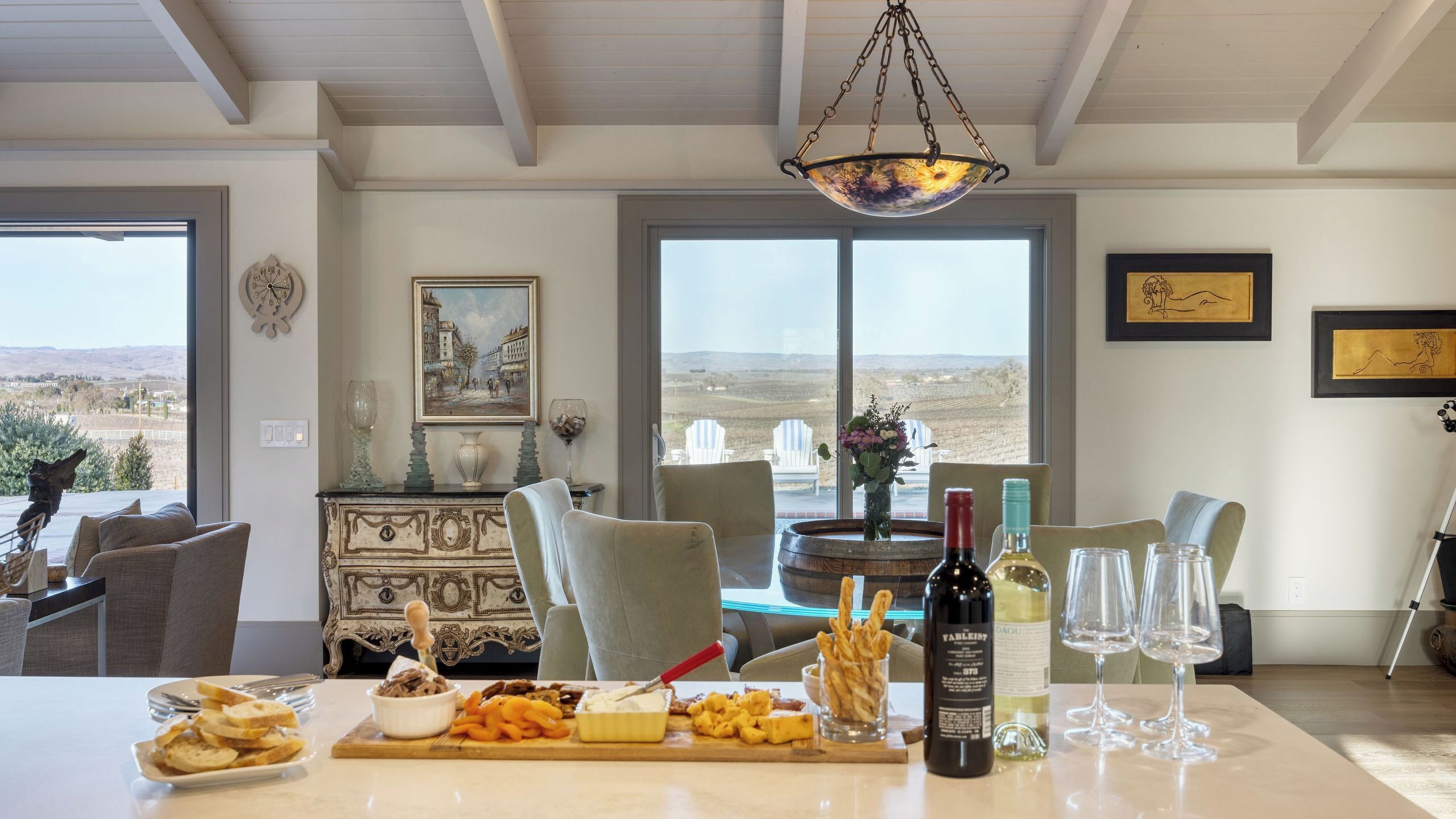 A dining area with a table set for a meal, a wine bottle, and a view of the countryside.