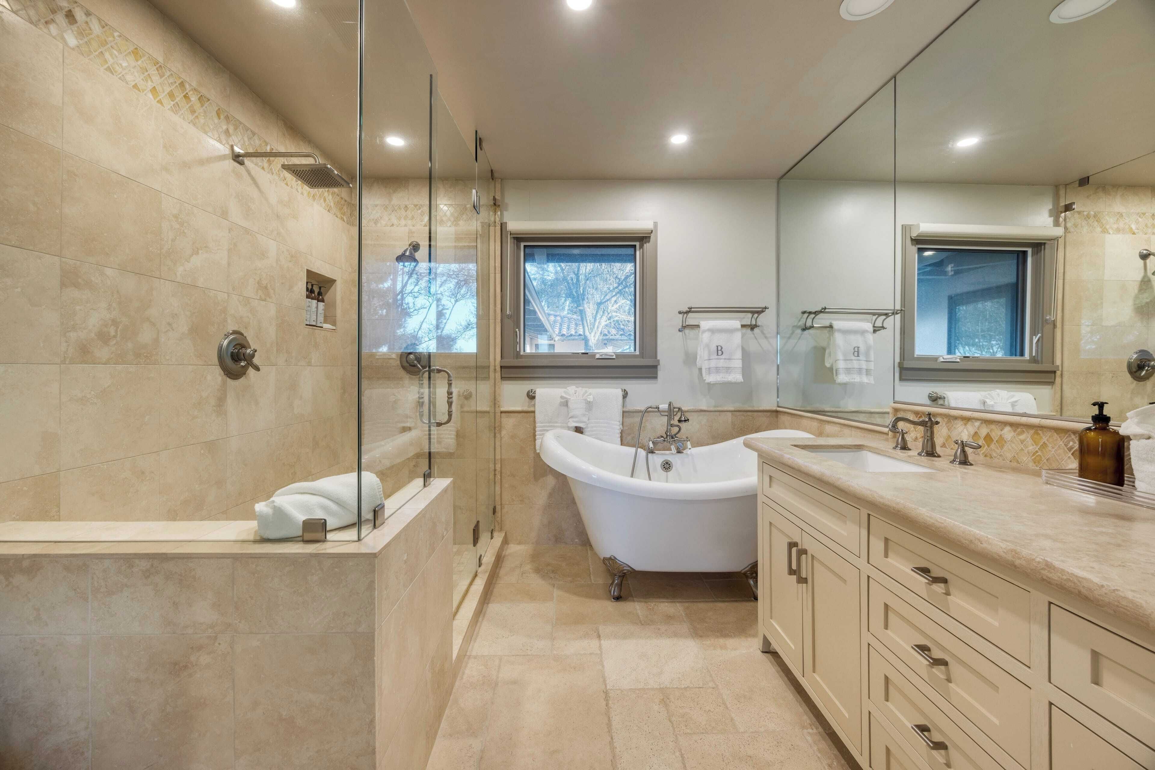 A modern bathroom with a glass-enclosed shower, a freestanding bathtub, and a large vanity with multiple sinks and drawers.