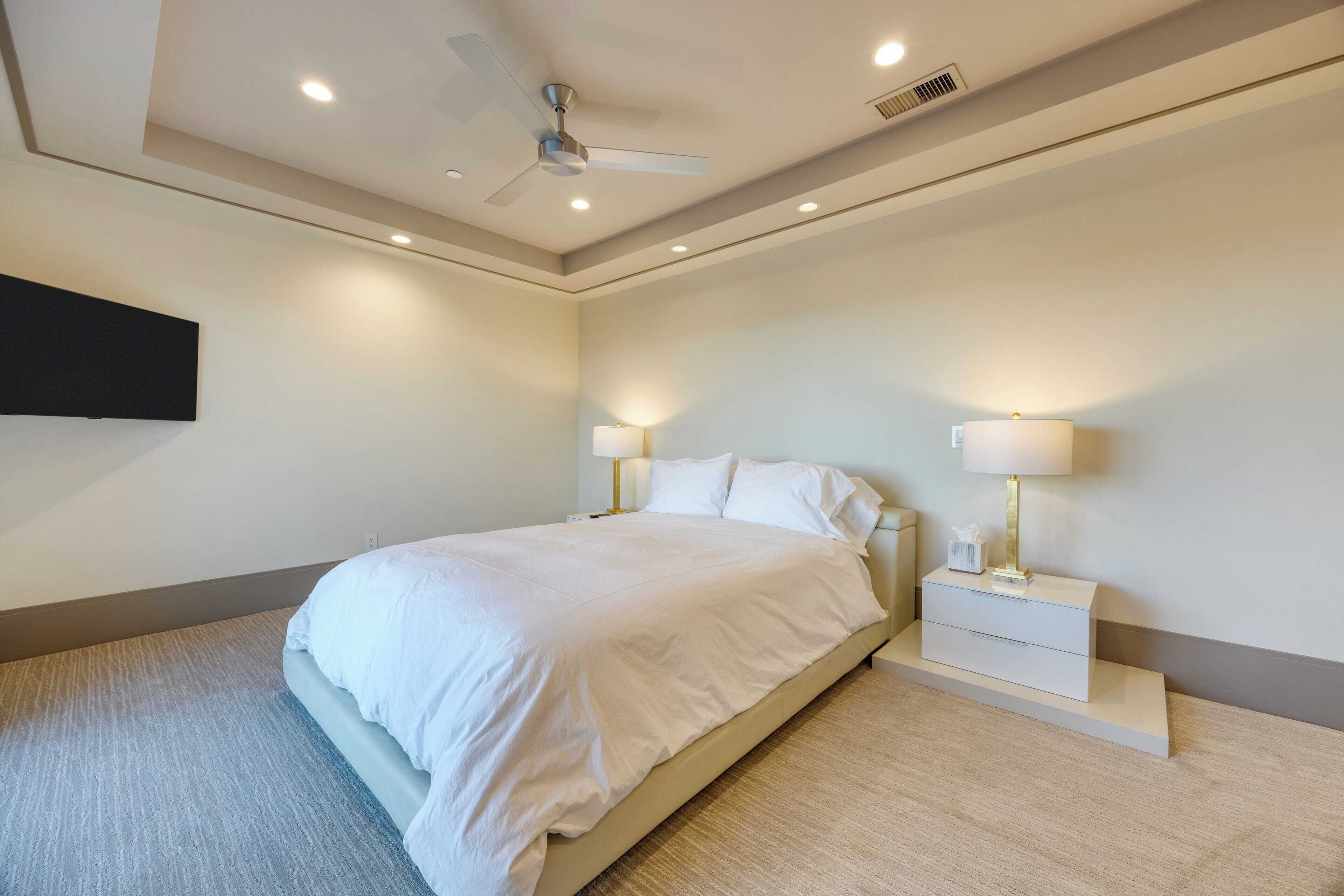 Ein modernes Schlafzimmer mit Bett, Nachttischen, Lampen und Deckenventilator.