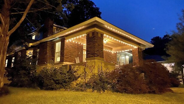 A two-story house with a brick facade, a covered porch with string lights, and a well-maintained lawn. - The Back House - Midtown Memphis Guest House with Private Entrance & Backyard (Memphis)