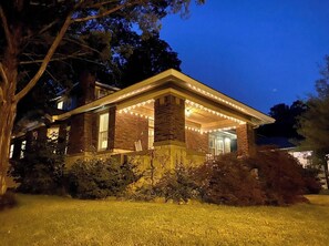 Une maison à deux étages avec une façade en briques, un porche couvert décoré de guirlandes lumineuses et une pelouse bien entretenue.