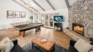 Amplia sala de estar con mesa de billar, asientos cómodos, chimenea de piedra y televisor.