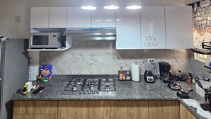 A kitchen with a granite countertop, white cabinets, a microwave, a gas stove, and hanging pendant lights.