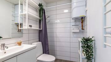 Un baño moderno con azulejos blancos, un lavabo blanco, un inodoro, una ducha con cortina morada y un estante blanco con una planta.