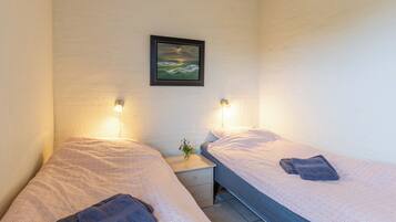 A twin room with two beds, each with a pillow and a folded towel. There is a small bedside table with a lamp and a framed picture on the wall.