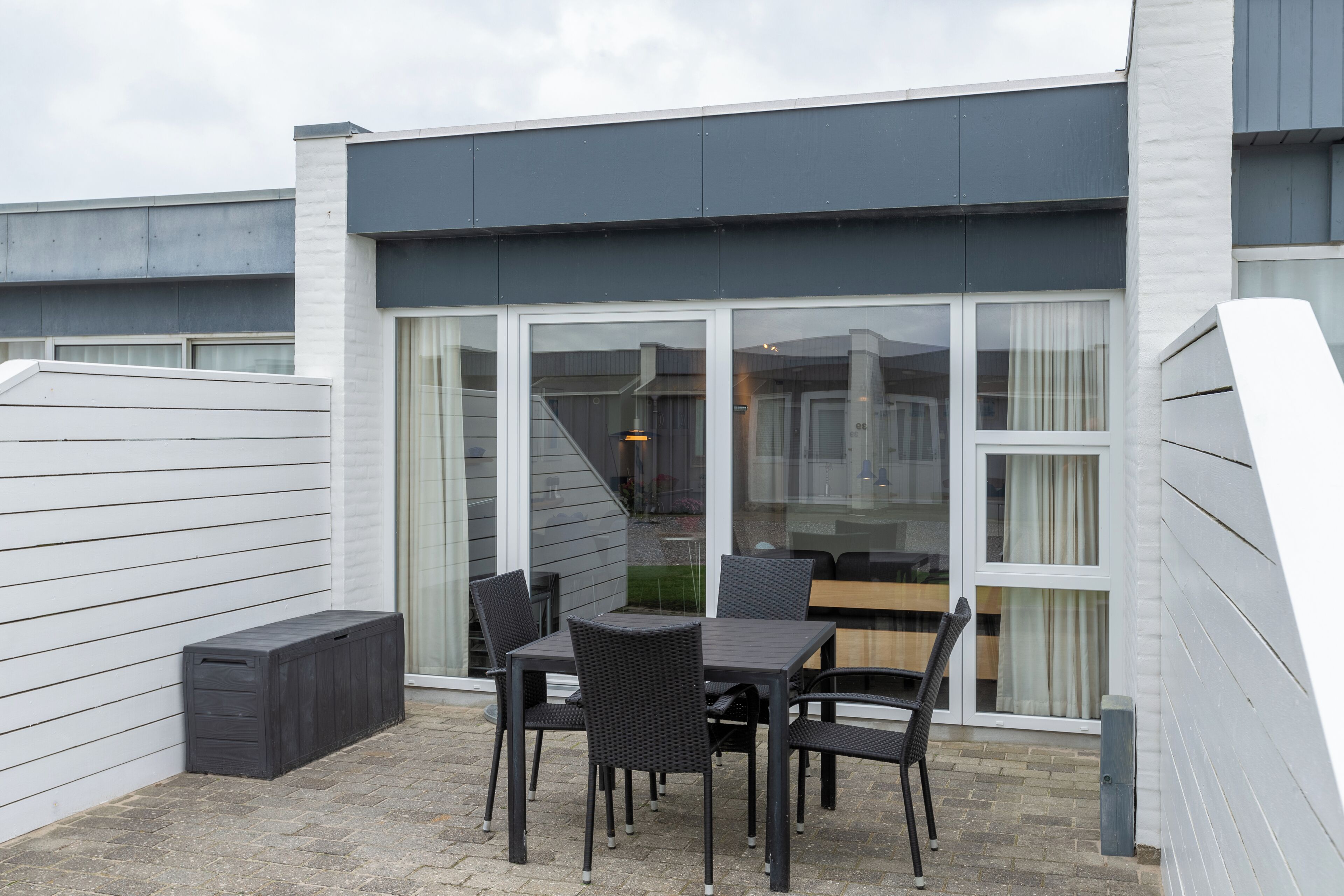Un patio con una mesa y sillas, un pequeño depósito de almacenamiento y una puerta corrediza de vidrio que da a un espacio interior.