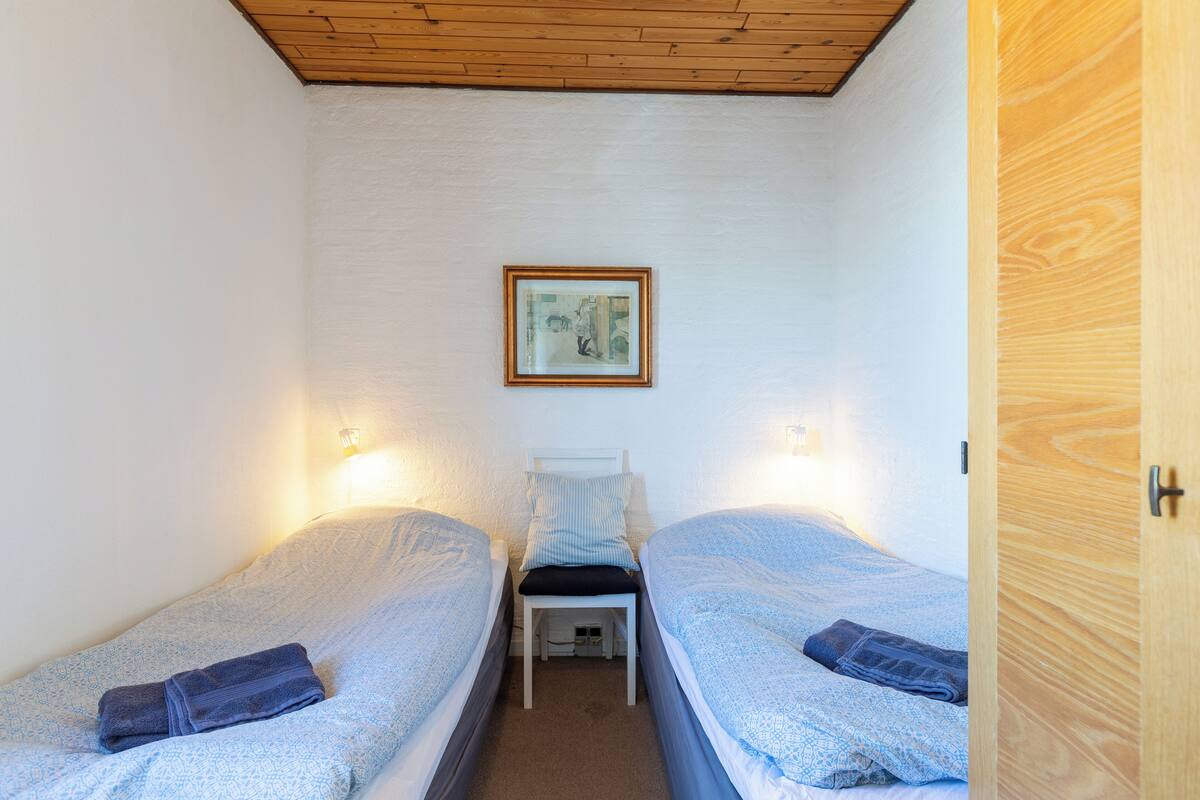 Ein kleiner, gut beleuchteter Raum mit zwei Einzelbetten, einer Holzbalkendecke und einem gerahmten Bild an der Wand.