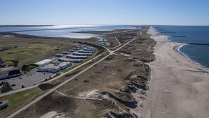 An aerial view of a coastal area with a row of buildings, a beach, and a water body. - Agger Holidays (Vestervig)