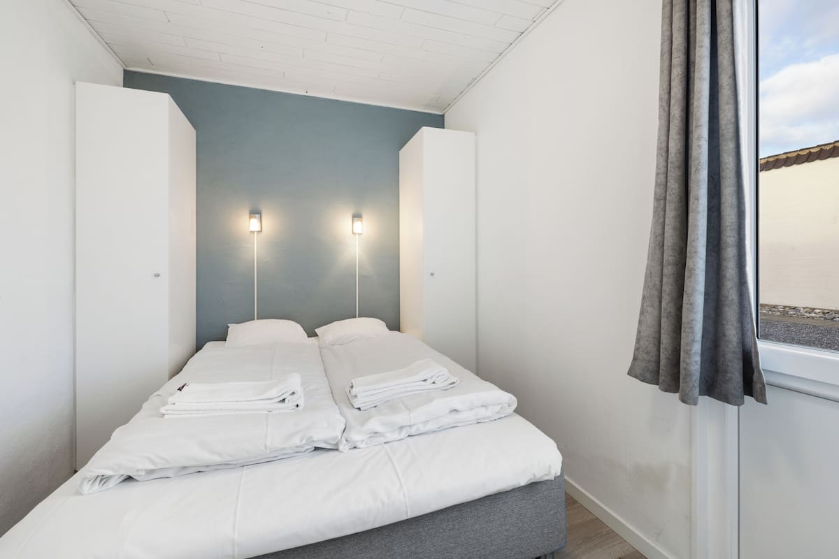 Ein modernes Schlafzimmer mit einem Bett, zwei Nachttischlampen und einem Fenster mit Vorhängen.