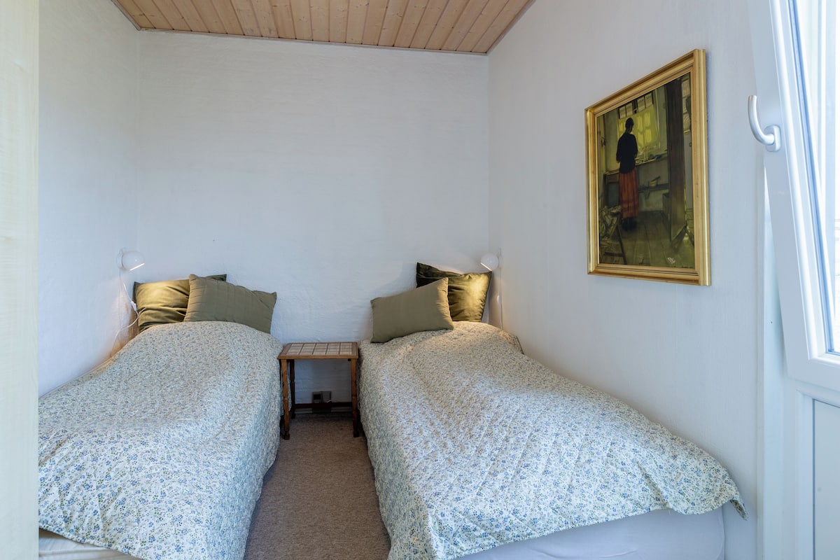 Ein kleiner, gut beleuchteter Raum mit zwei Einzelbetten, einem Nachttisch und einem Bild an der Wand.