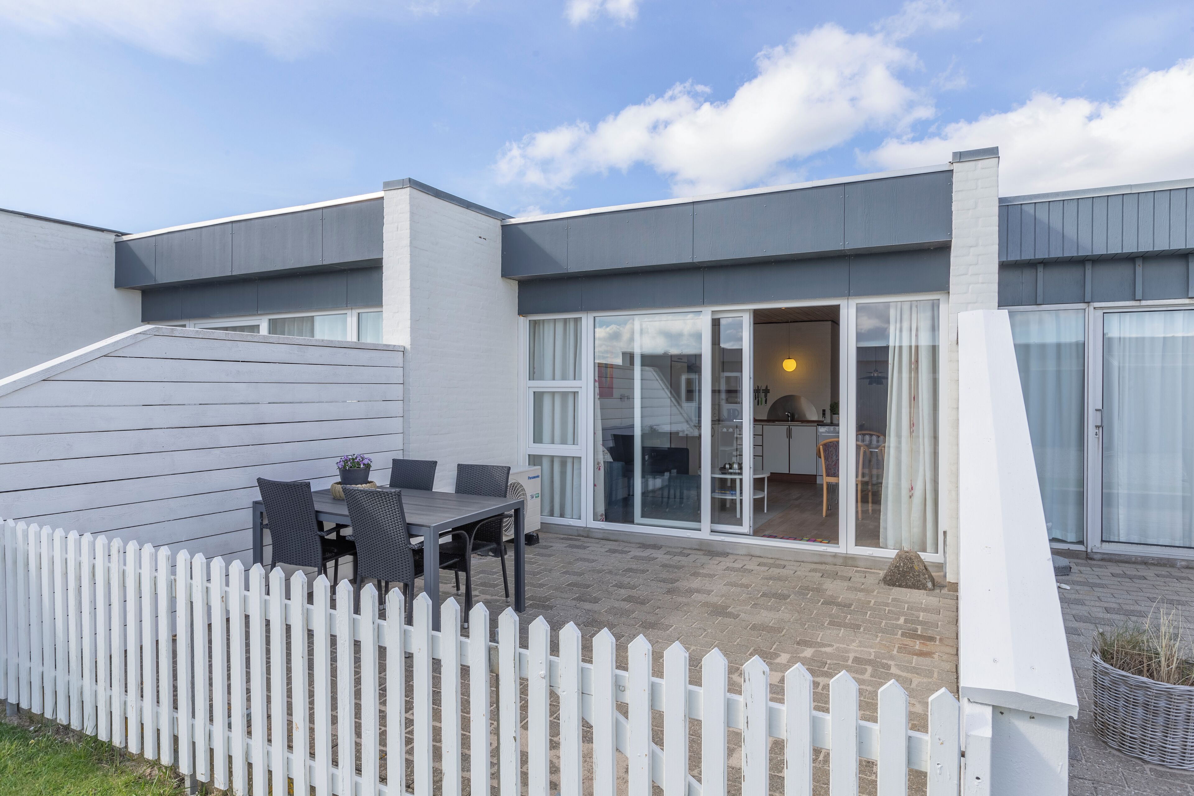 A modern house with a patio, white picket fence, and a dining area with a table and chairs.