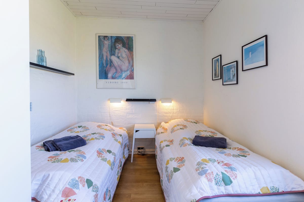 Ein Zimmer mit zwei Betten, einem kleinen weißen Tisch und einem an der Wand befestigten Regal.
