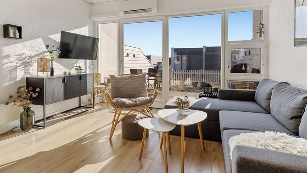 A modern living room with a grey sofa, a round white table, and a wicker chair. - Agger Holidays (Vestervig)