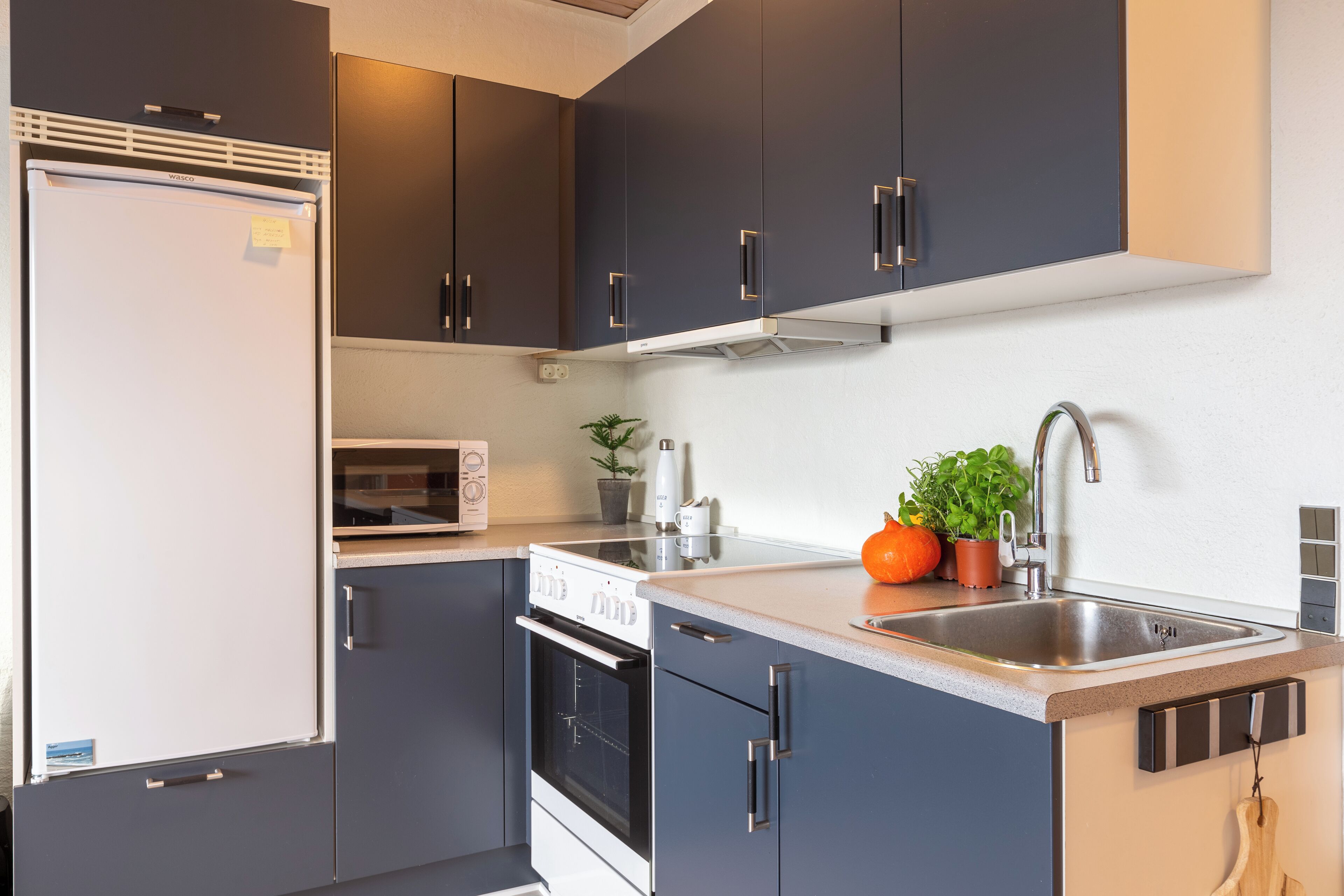 A modern kitchen with dark cabinets, a built-in oven, a microwave, and a stainless steel sink.