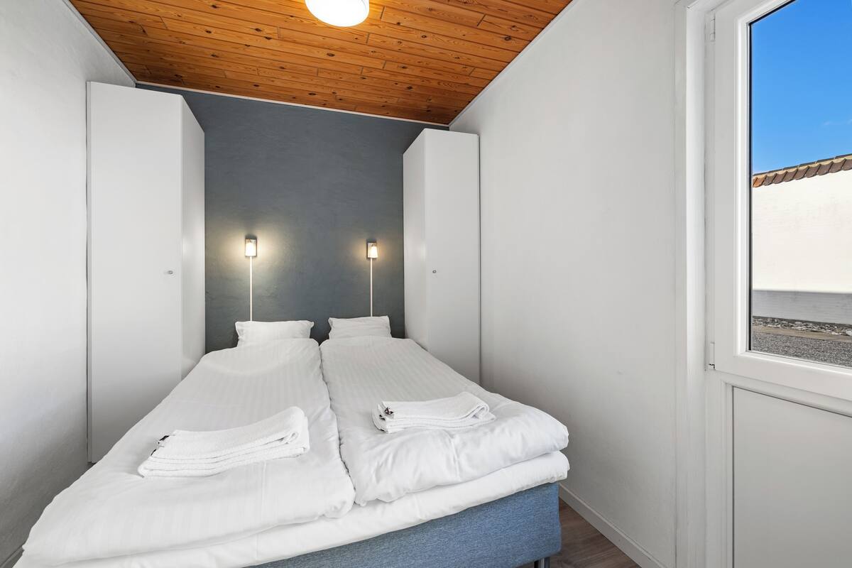 Ein Einzelbett mit weißer Bettwäsche und Handtüchern, eine Holzzieldecke und zwei Wandleuchten.