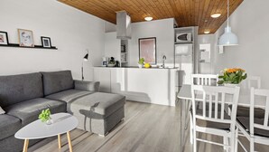 A modern living space with a grey sofa, a small round table, and a dining area with white chairs. - Agger Holidays (Vestervig)